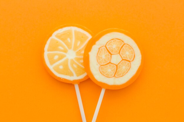 High angle view of fresh sweet citrus fruit lollipops on orange surface