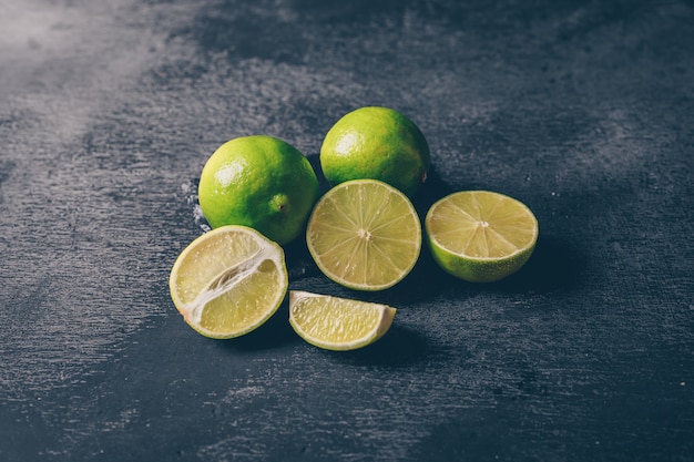 High angle view green lemons with slices on black textured background. horizontal