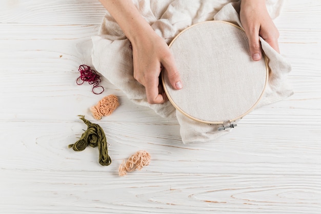 High angle view of hand holding hoop with colorful thread over white wooden table