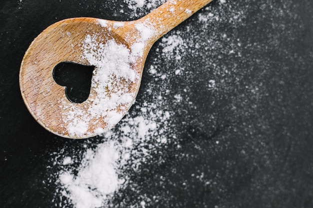 Free photo high angle view of heart shape spoon and flour on black background