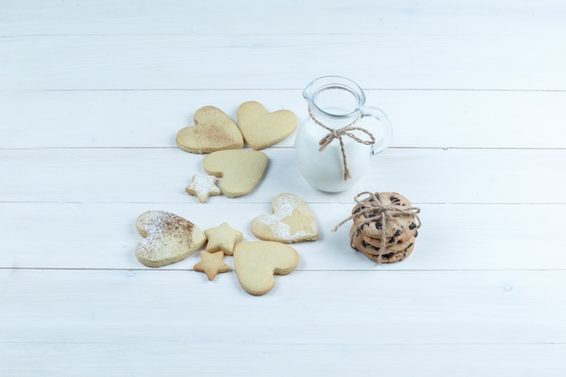 High angle view heart shaped and star cookies with jug of milk on white wooden board background. horizontal