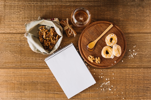 High angle view of honey; donut; walnut; cinnamon and spiral notepad on wooden desk