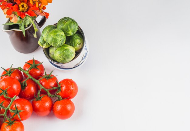 High angle view of juicy tomatoes; brussels sprouts and flowers on white background