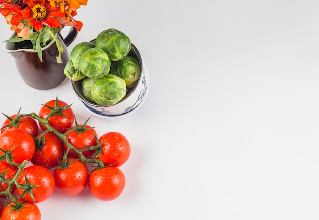 High angle view of juicy tomatoes; brussels sprouts and flowers on white background