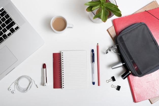 High angle view of laptop; makeup pouch; earphone and coffee cup and files over white desk