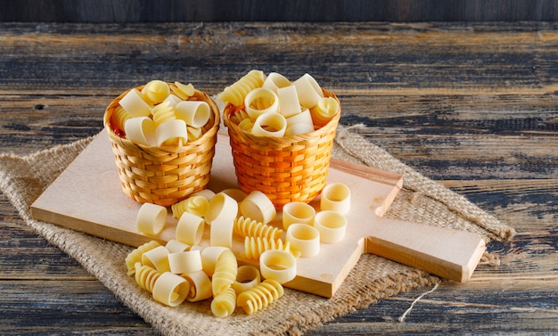 High angle view macaroni pasta in buckets on sackcloth, cutting board and wooden background. horizontal