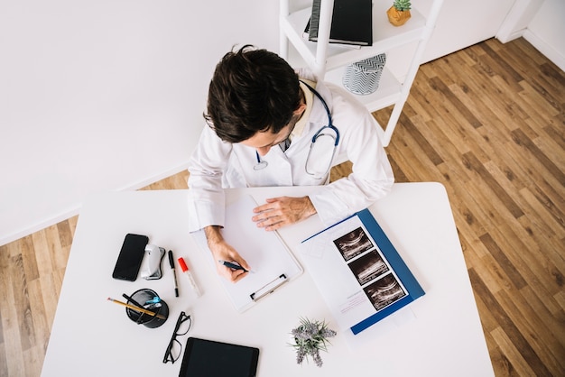 Free photo high angle view of a male doctor writing on clipboard in clinic