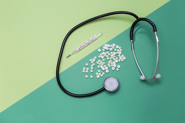 High angle view of medicines; thermometer and stethoscope on dual colored background