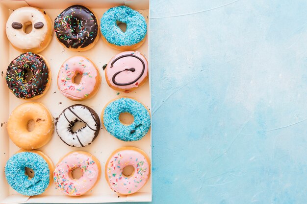 High angle view of multi colored fresh donuts in box on blue background