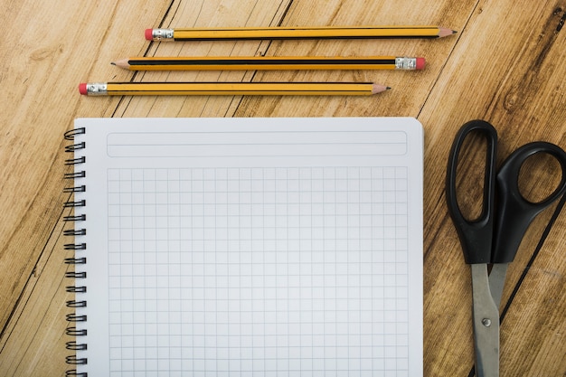 High angle view of notepad; scissors and pencils on wooden backdrop