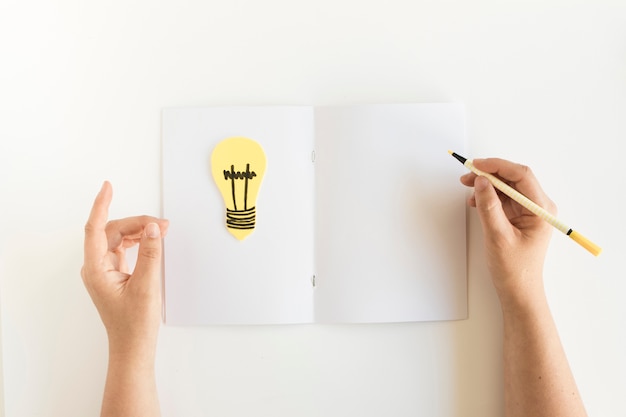 Free Photo high angle view of a person's hand writing on card with light bulb