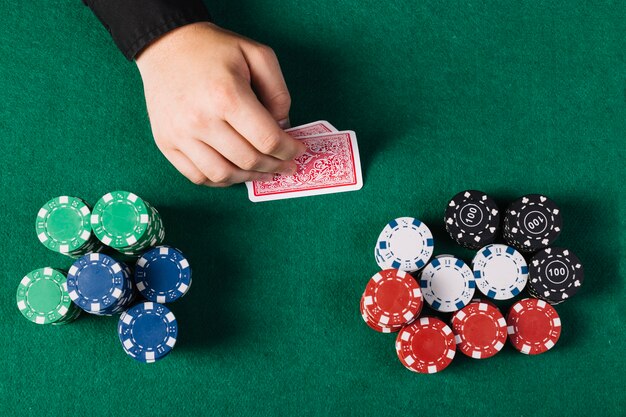 High angle view of player's hand with playing cards near poker table