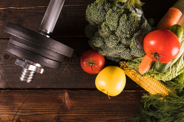 High angle view of raw vegetables and dumbbells on wooden background