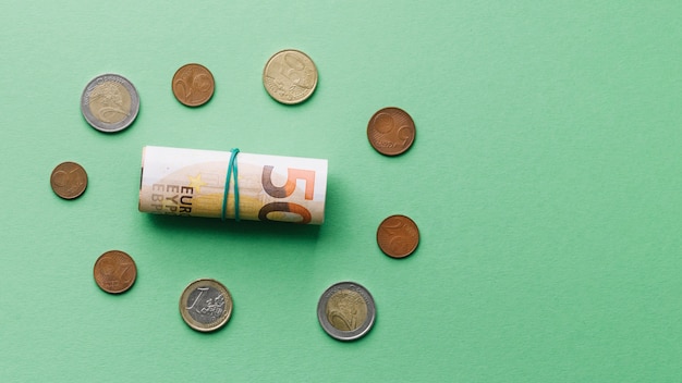 Free photo high angle view of rolled up euro bank note with coins on green background