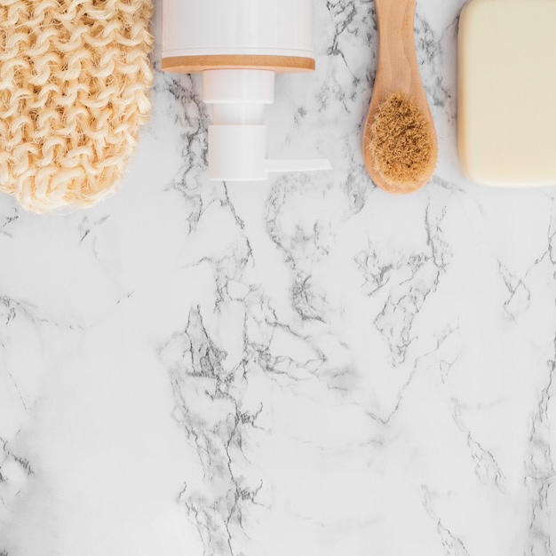 High angle view of scrub glove; cosmetic bottle; soap and brush on marble surface