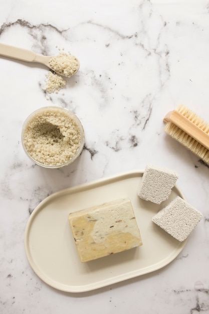 High angle view of soap; salt; pumice stone and brush on marble surface