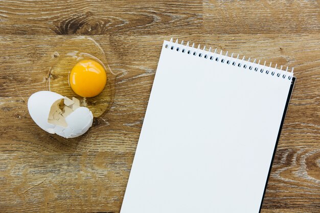 High angle view of spiral notepad and egg on wooden desk