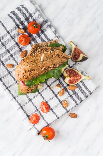 Free Photo high angle view of tasty hot dog; fresh fig slices; almonds and cherry tomatoes on napkin over white backdrop