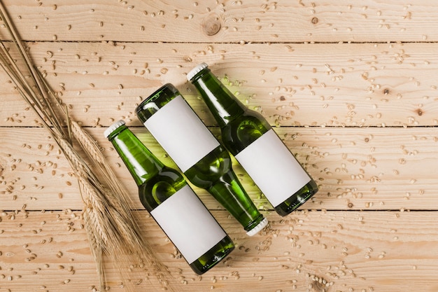 High angle view of three beer bottles and ears of wheat on woodgrain