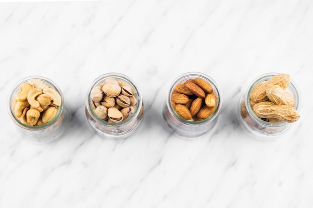 Free photo high angle view of various nut food jar on marble background