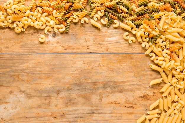 High angle view of various types of uncooked pasta on wooden desk