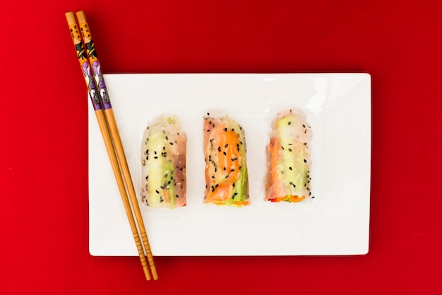 Free photo high angle view of vegetable rice spring rolls decorated with sesame seeds on white plate with wooden chopsticks