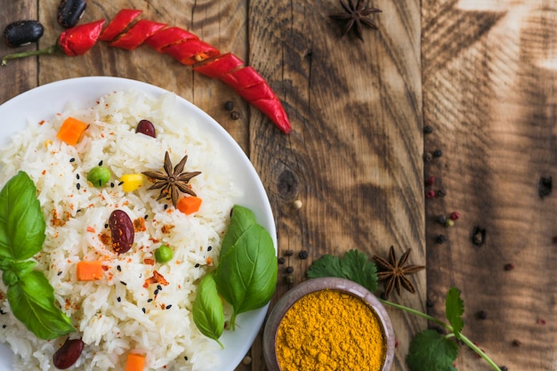 Free photo high angle view of vegetable rice; turmeric powder; red chili pepper and dry spices over wooden backdrop