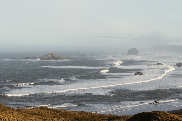 Free photo high angle view of the wavy sea surrounded by rocks covered in the fog at daytime