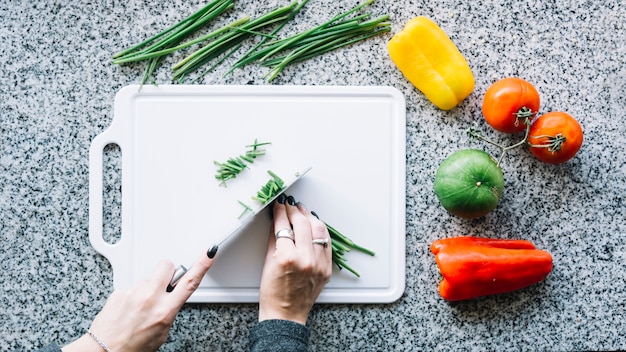 Free Photo high angle view of a woman's hand cutting scallion on chopping board