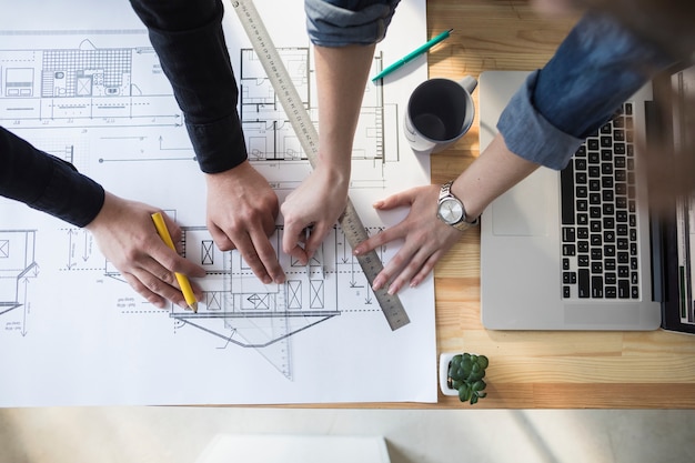 Free Photo high angle view of worker's hand working on blueprint over wooden table at workplace