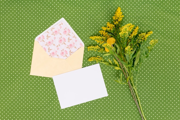 High angle view of yellow goldenrod flowers with card; open envelope above green textured background