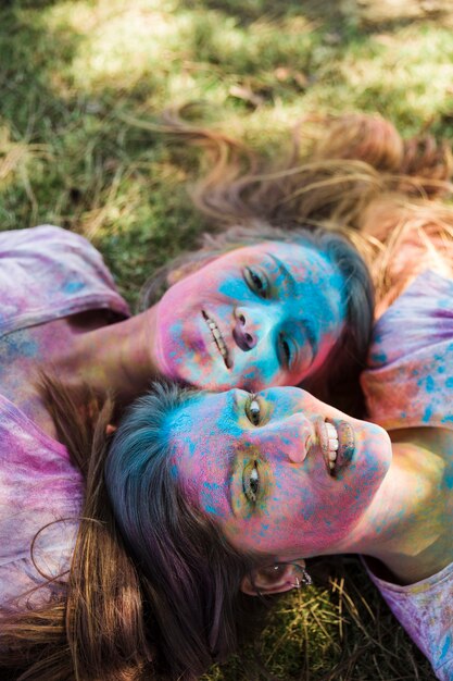 High angle view of young women with holi color on their face lying on lawn looking at camera