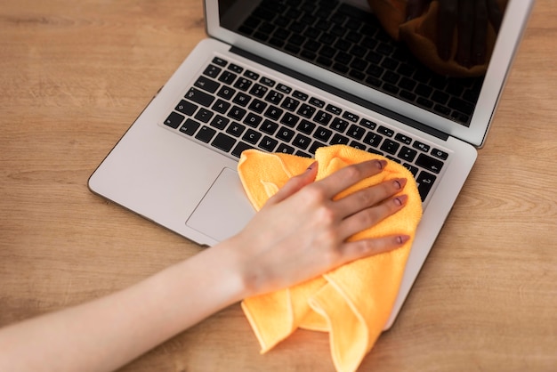 High angle of woman cleaning laptop with cloth