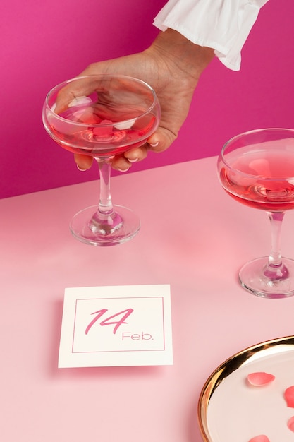 Free photo high angle of woman's hand holding drink glass next to valentines day card and rose petals