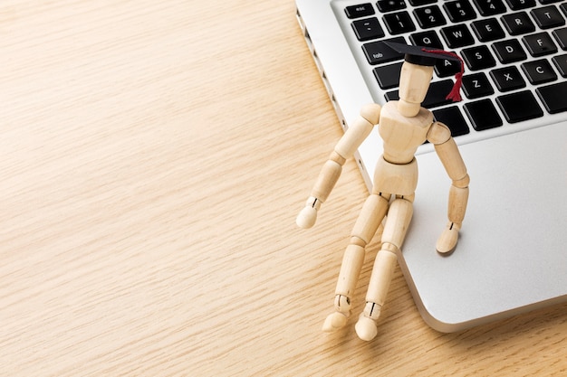 High angle of wooden figurine with academic cap and laptop