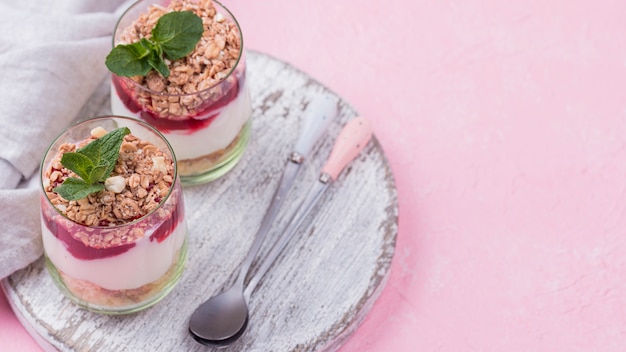 High angle of yogurt glasses with cereal and spoons