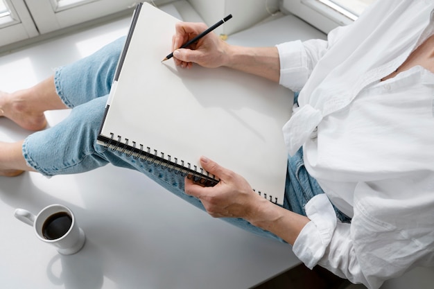 Free Photo high angle of a young woman drawing at home near the window