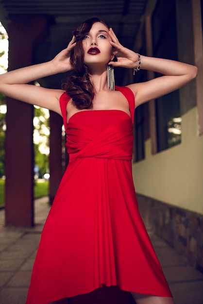 Free photo high fashion look.glamor closeup portrait of beautiful sexy stylish brunette caucasian young woman model with bright makeup, with red dark lips, in bright summer red evening dress outdoors