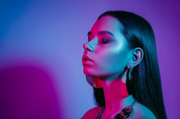 High fashion model in colorful bright neon lights posing at studio. Portrait of beautiful girl with trendy glowing make-up. Art design vivid style.