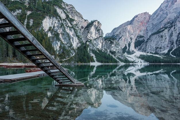 Free photo high rocky mountains reflected in braies lake with wooden stairs near the pier in italy