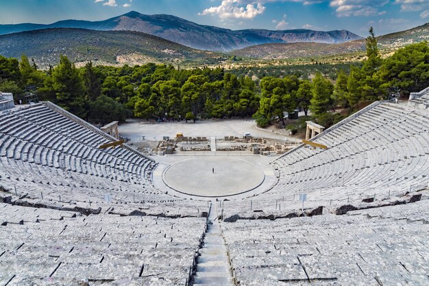 High shot of an amphitheater made out of stone with green trees and mountains in the background