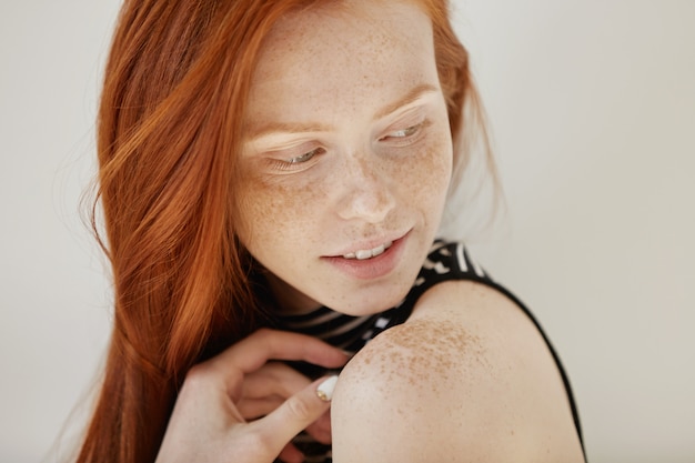 Free photo highly-detailed shot of tender and cute teenage female with shy faint smile, loose ginger hair and and clean heathy skin looking over her shoulder