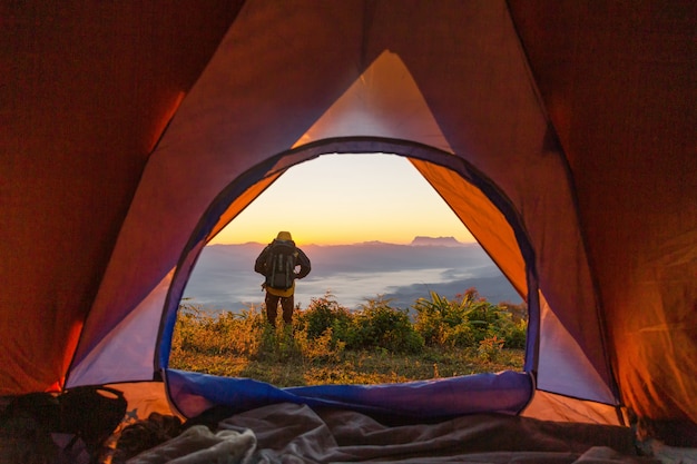 Hiker stand at the camping near orange tent and backpack in the mountains