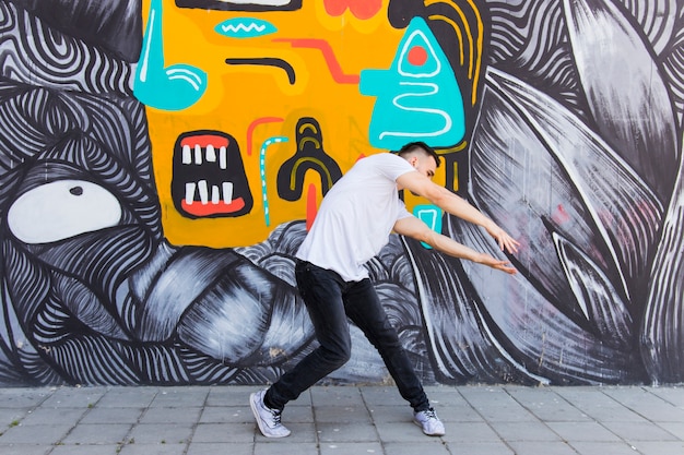 Free photo hip hopper performing dance in front of graffiti wall