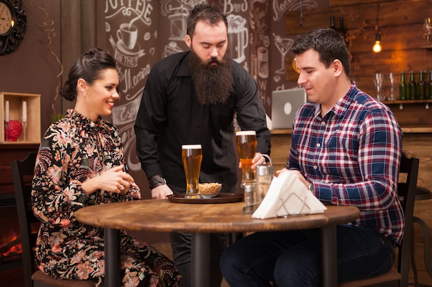 Free photo hipster barman giving the order to beautiful young couple.great pub.