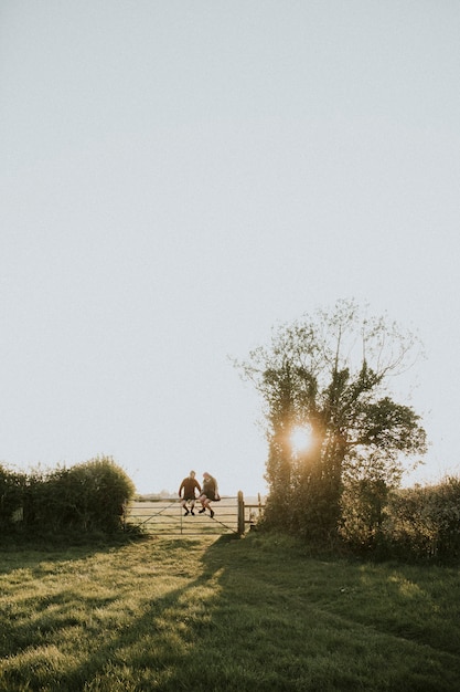 Free photo hipster couple sitting on a gate together in the countryside