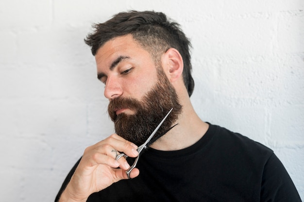 Free photo hipster male cutting beard with scissors