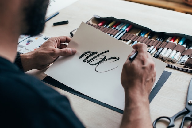 Free Photo hipster young illustrator artist in black simple tshirt creates authentic and unique hand lettering drawing in his bright industrial studio