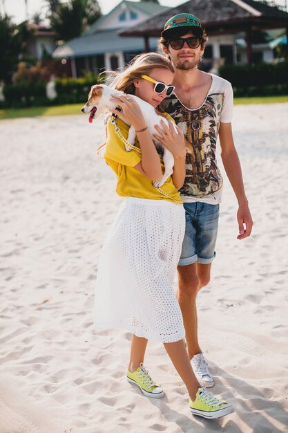 Hipster young stylish hipster couple in love walking and playing with dog in tropical beach