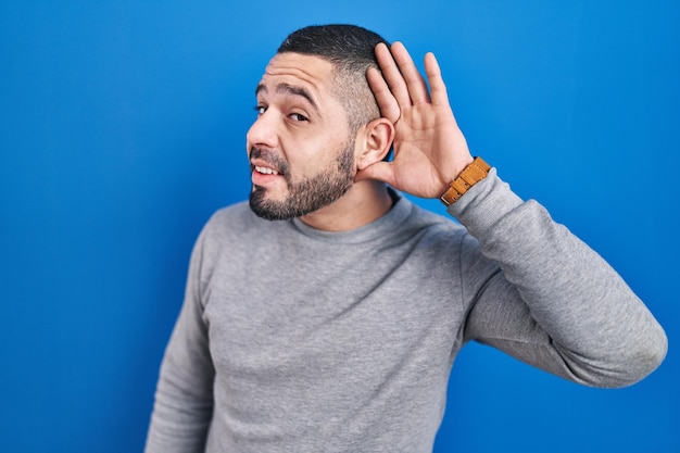 Free Photo hispanic man standing over blue background smiling with hand over ear listening an hearing to rumor or gossip deafness concept